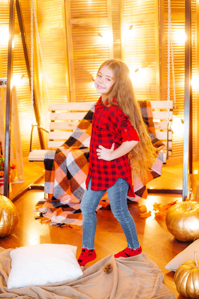 Cute little girl with long hair in a red checkered shirt in autumn scenery with pumpkins and yellow leaves in the  - Foto, Imagem