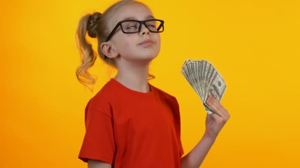 Little smart girl rejoicing first money, waving bunch of dollars and smiling - Кадри, відео