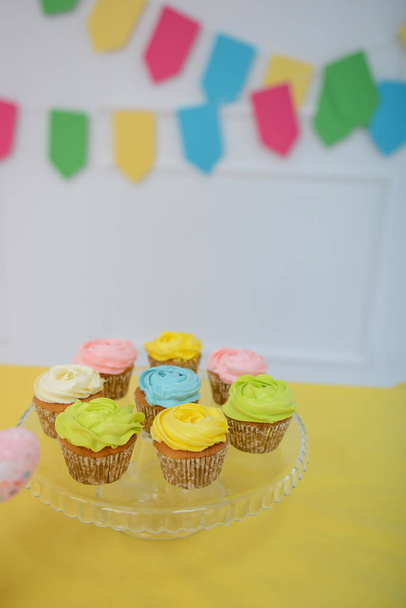 Beautiful multi-colored cupcakes. The room is decorated with bright decor. Close-up. - Foto, afbeelding