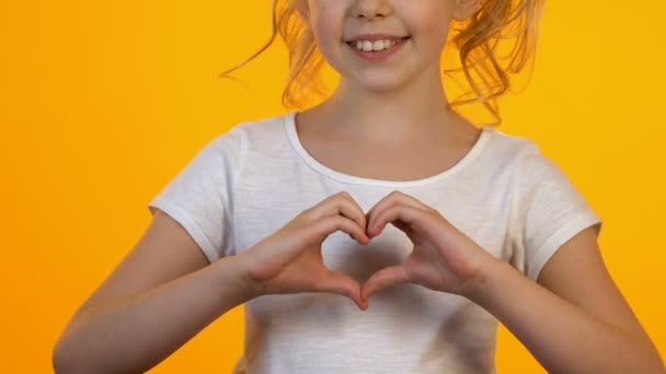 Mała kobieta dziecko pokazując znak serca z rąk, uśmiechając się na aparat fotograficzny, koncepcja miłości - Materiał filmowy, wideo
