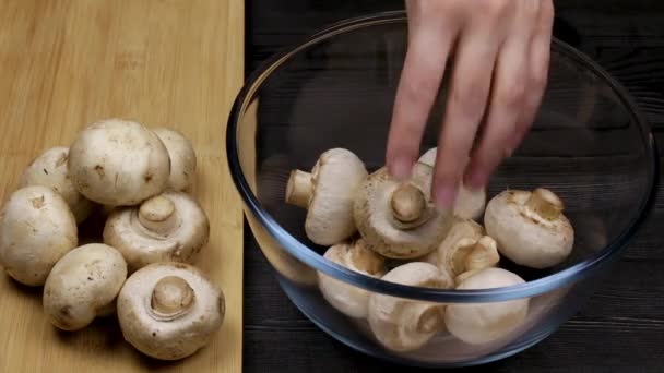 Chief cook puts his peeled champignons in a glass bowl next to a pile of mushrooms on a cutting board. - Footage, Video