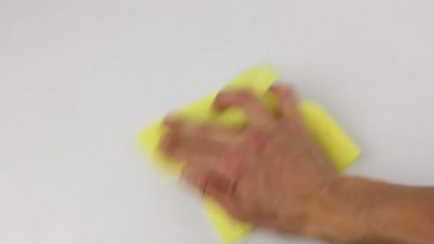 ihmiskäsi pyyhkii varovasti pöydän valkoisen pinnan keltaisella neliökankaalla
 - Materiaali, video