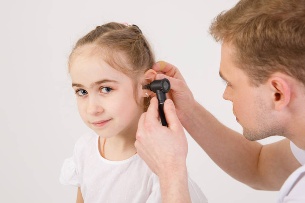 O jovem otorrinolaringologista simpático examina os ouvidos de uma menina - uma menina em idade escolar. Pessoas isoladas em um fundo branco
 - Foto, Imagem