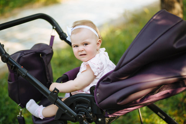 Cute little beautiful baby girl of 6 months sitting in the pram or stroller and waiting for mom - Foto, Bild