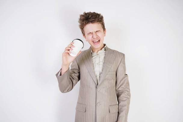 fáradt tini fiú szürke öltöny, papír csésze kávé a kézben fehér stúdió háttér - Fotó, kép