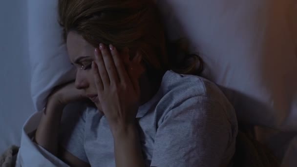 Crying woman lying in bed at night, holding head, suffering from migraine - Footage, Video