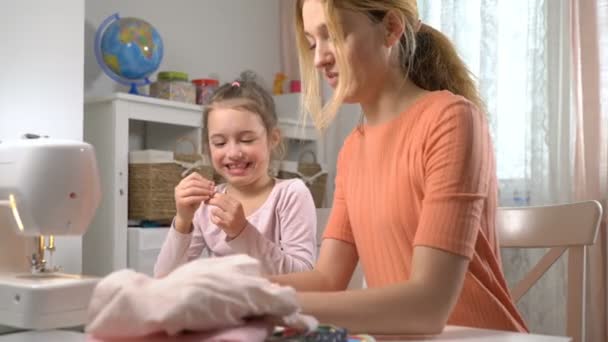 Mom teaching her little daughter to sew using needle and thread - Materiał filmowy, wideo