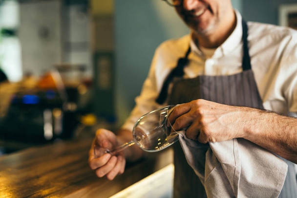 カフェバーでワイングラスを磨く成熟したバーマン - 写真・画像