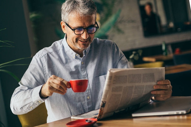 Smiling businessman reading newspaper and drinking coffee in modern cafe bar. - Zdjęcie, obraz