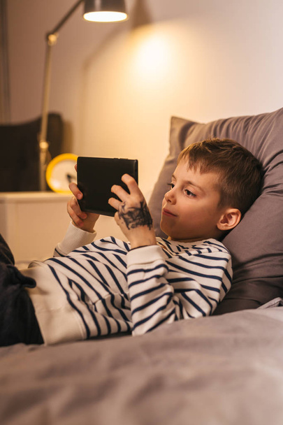 Happy boy using tablet at home laying on bed - 写真・画像