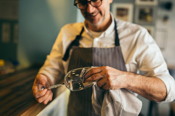 Mature barman polishing wine glass in cafe bar - Fotoğraf, Görsel