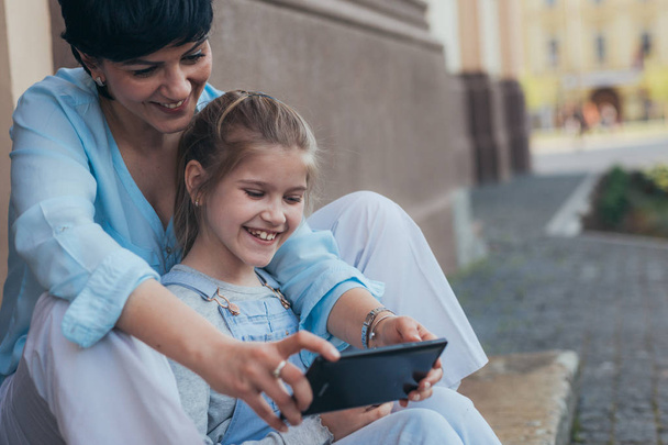 Mother and daughter using tablet outdoor in the city, sitting on stairs. - Zdjęcie, obraz
