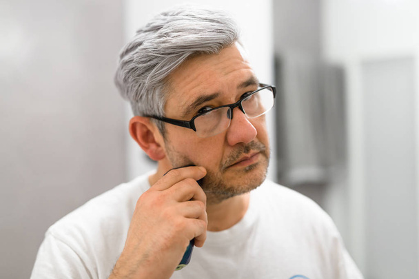 Portrait d'homme aux cheveux gris rasant la barbe avec rasoir électrique
 - Photo, image