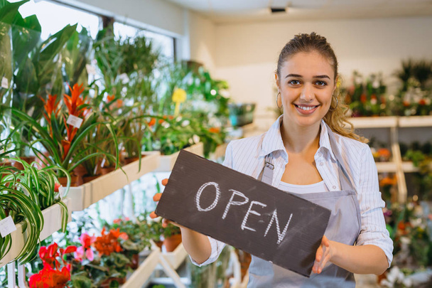 Woman entrepreneur holding open signboard in flower shop - Фото, изображение