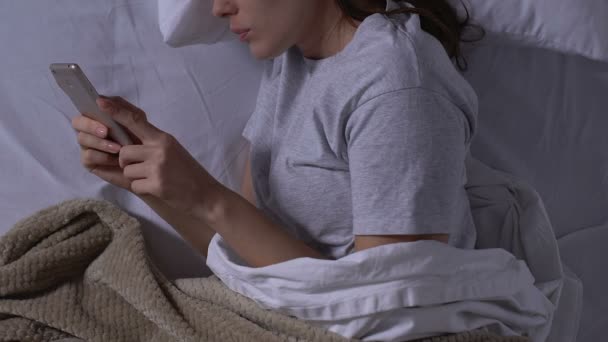 Woman chatting with boyfriend on smartphone, lying in bed at night, relations - Záběry, video
