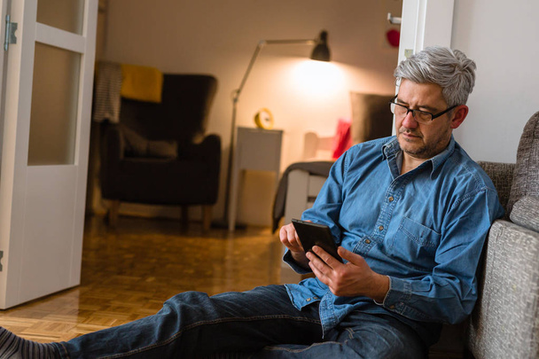 Middle aged gray haired man using tablet at his apartment - Foto, Imagem