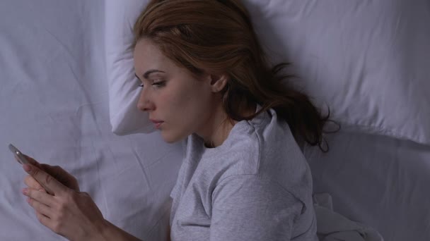 Happy lady chatting on smartphone with beloved, lying in bed, tender relations - Imágenes, Vídeo