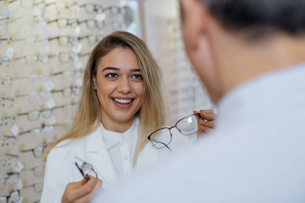 Woman optician helping male customer to find best eyeglasses - Fotoğraf, Görsel