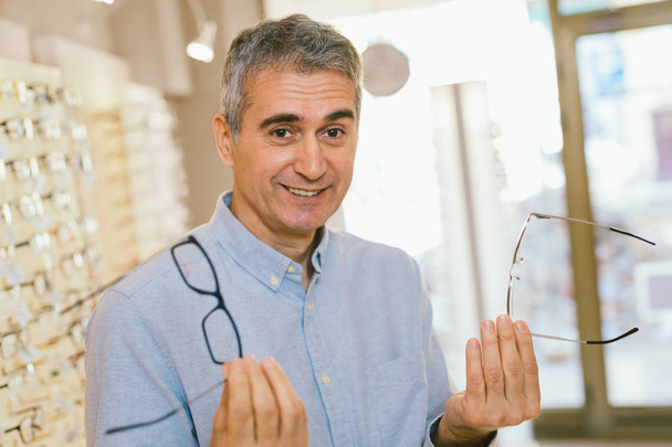 man choosing the best glasses for him in optics store - Foto, Bild