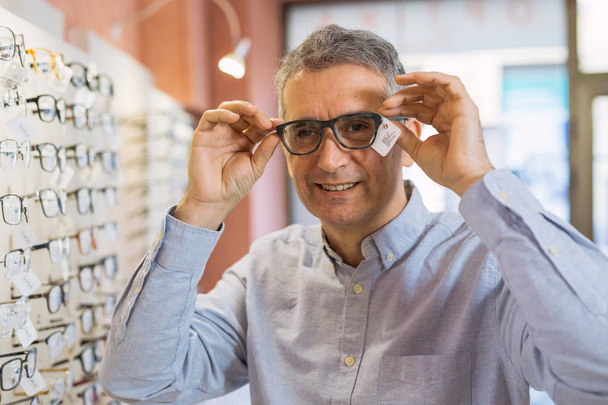 Mature man choosing eyeglasses in optic store - Foto, Imagem