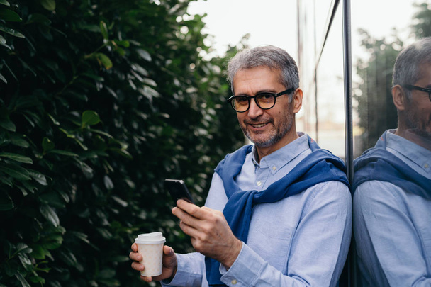 Man walking outdoor using cellphone and drinking coffee - Photo, image