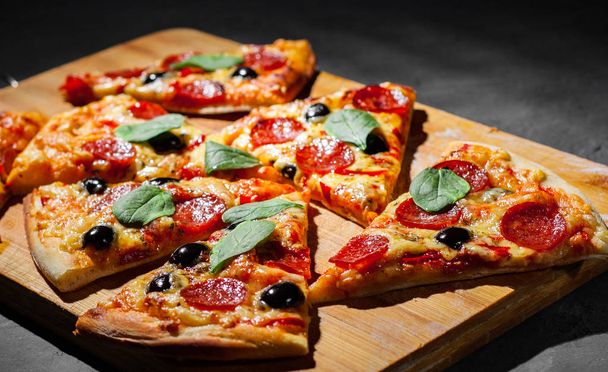 Pepperoni Pizza with Mozzarella cheese, salami, olive, pepper, Spices and Fresh spinach. Italian pizza on Dark grey black slate background - Фото, изображение