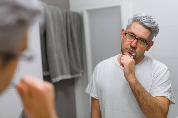 Сонний чоловік чистить зуби у ванній
 - Фото, зображення