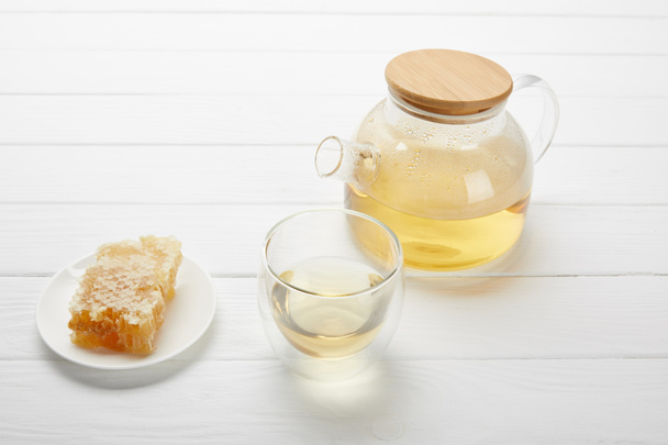 čajový hrnec s organickým bylinkovým čajem, skleněným a voštovým hřebenem na bílém dřevěném stole - Fotografie, Obrázek