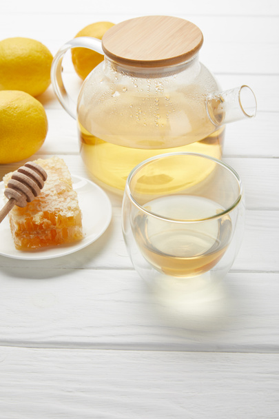 teáskanna bio gyógytea, üveg, citrom és méhsejt a fehér fából készült asztal - Fotó, kép