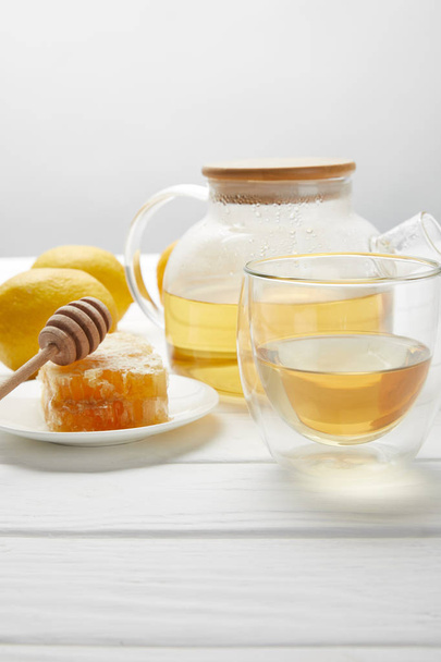 teapot with organic herbal tea, glass, lemons and honeycomb on white wooden table  - Fotó, kép