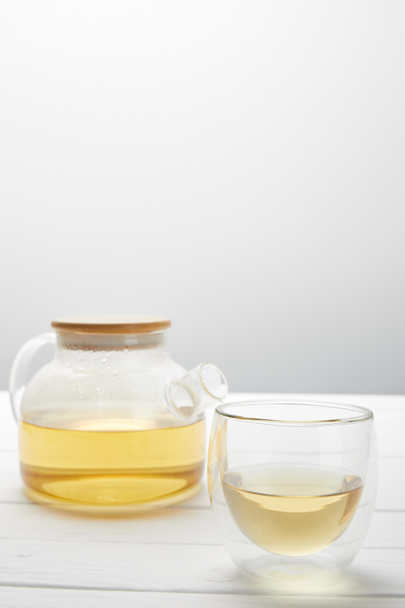 teapot with organic herbal tea and transparent glass on grey with copy space - Photo, image