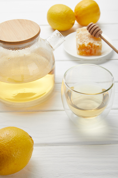 transparent teapot with green tea, fresh lemons and honeycomb on white wooden table - Fotoğraf, Görsel