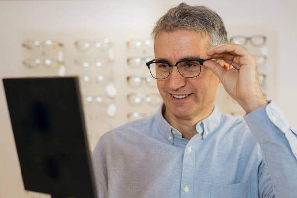 Mature man choosing eyeglasses in optic store - Foto, afbeelding