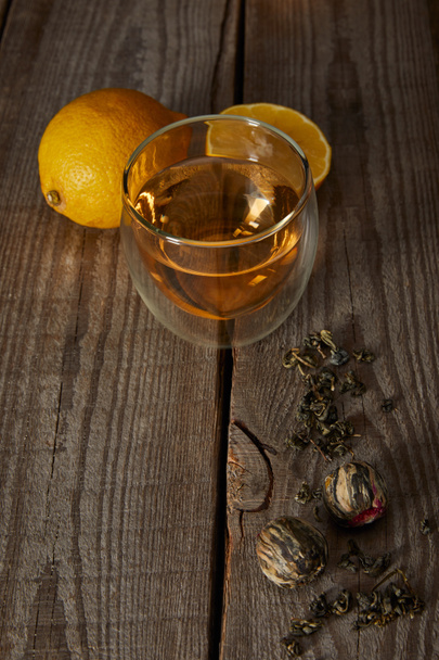 glass of traditional chinese blooming tea, lemons and tea balls on wooden table  - Zdjęcie, obraz
