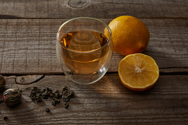 glass of traditional chinese blooming tea, lemons and tea balls on wooden table  - Foto, afbeelding