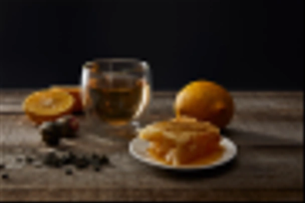 transparent glass with blooming tea, honeycomb and lemons on wooden table isolated on black - Photo, Image