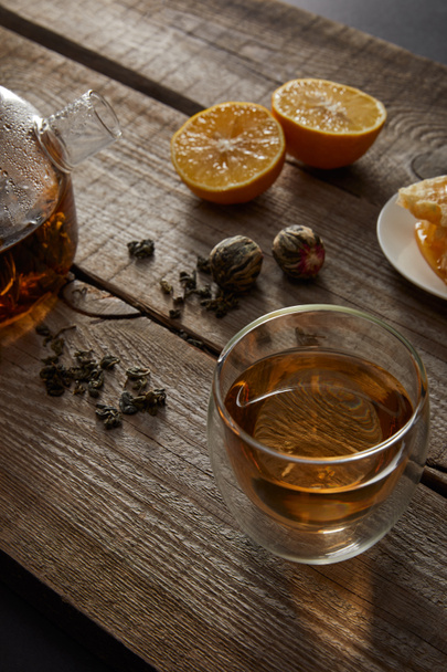 tetera transparente con vaso de té chino en flor, bolas de té y limones en la mesa de madera
 - Foto, Imagen
