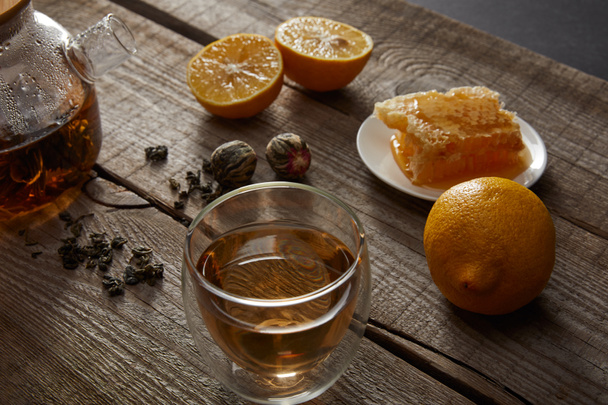 átlátszó teáskanna üveg kínai virágzó tea, méhsejt, tea labdák és citrom, fából készült asztal - Fotó, kép