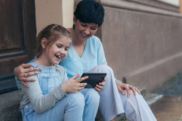 little girl using tablet with mom outdoor in the city - Foto, Imagem