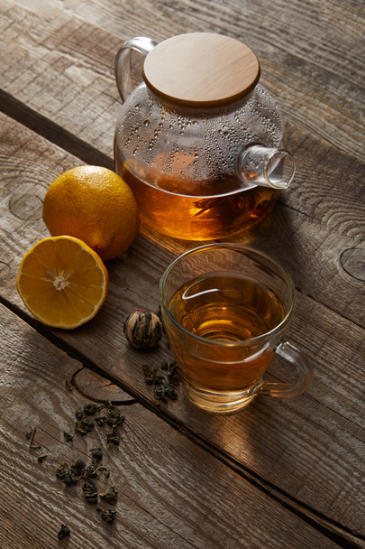 átlátszó teáskanna a pohár hagyományos kínai virágzó tea és a citrom a fa felületén - Fotó, kép