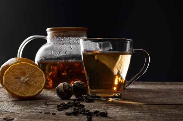 transparent teapot and cup with traditional blooming tea on wooden table with lemons isolated on black - 写真・画像