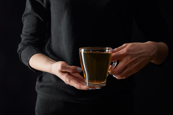 vista recortada de mujer joven sosteniendo taza transparente de té verde aislado en negro
 - Foto, Imagen