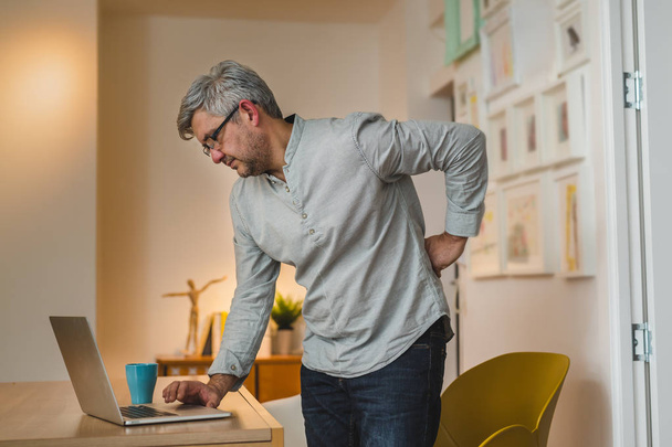 Mature gray haired man having backache while working laptop at home - Valokuva, kuva