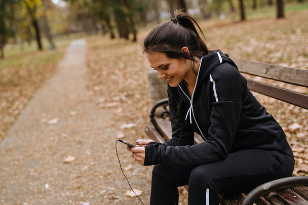 giovane donna che fa jogging seduta sulla panchina nel parco cittadino e usando il suo smartphone
 - Foto, immagini