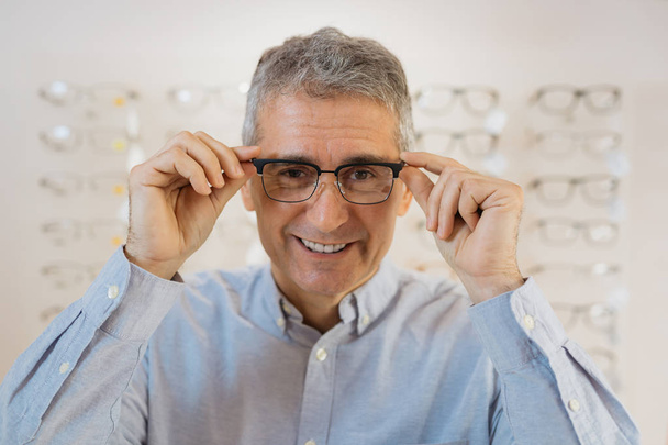 Man trying on eyeglasses for best vision in optic store - Foto, Imagem