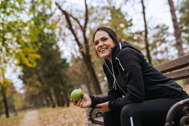 Sportswoman eating apple in city park sitting o bench - 写真・画像