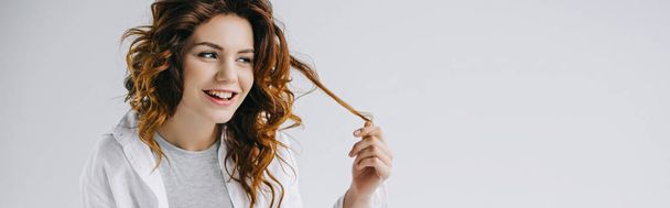 panoramic shot of cheerful young woman touching red hair on white  - Foto, afbeelding