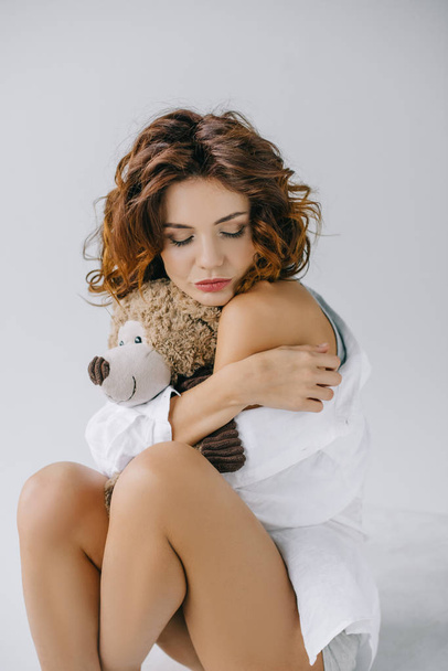 pretty curly young woman holding teddy bear while sitting on white  - Фото, зображення