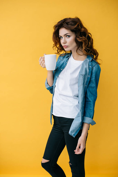 attractive young woman with curly red hair holding cup on orange  - 写真・画像