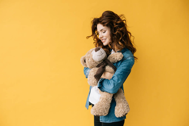 fröhlich lockige junge Frau hält Teddybär auf Orange  - Foto, Bild